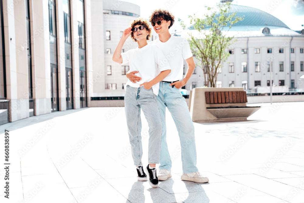 Young smiling beautiful woman and her handsome boyfriend in casual summer white t-shirt and jeans clothes. Happy cheerful family. Female having fun. Couple posing in street at sunny day. In sunglasses