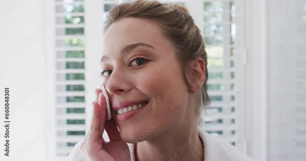 Happy biracial woman cleansing face using cotton pad in bathroom, slow motion Happy biracial woman cleansing face using cotton pad in bathroom, slow motion
