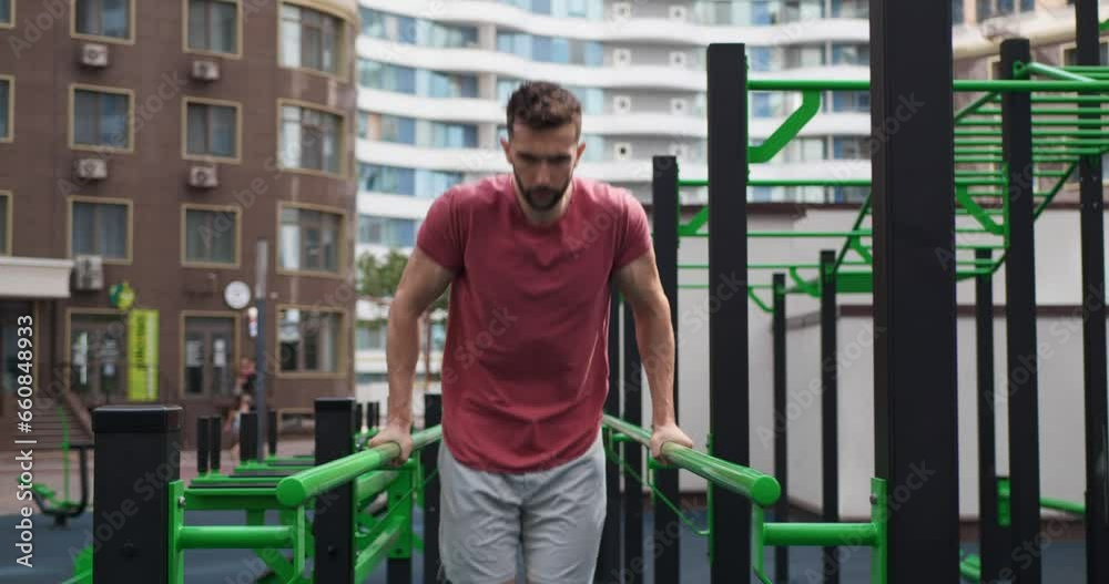 Athletic man doing dips at outdoor gym, low angle view. Camera moving backward and forward