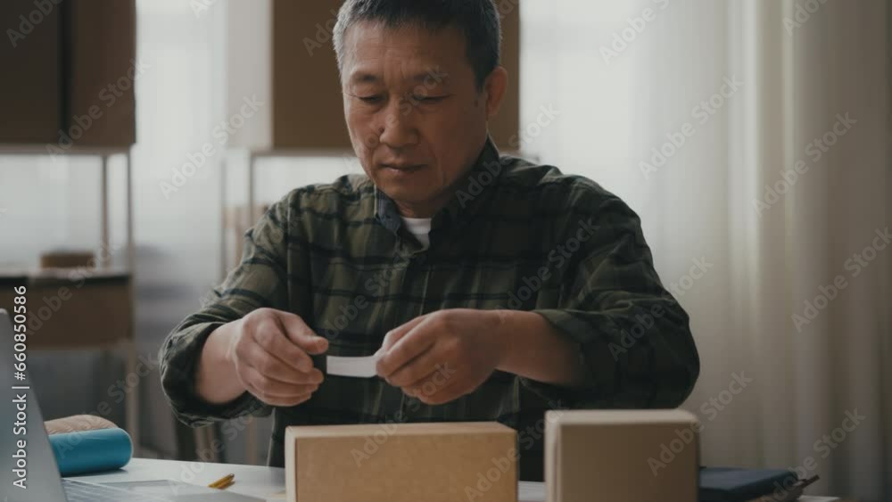 Small business owner fills invoice, adds sticker to box, packs order for client Small business owner fills invoice, adds sticker to box, packs order for client