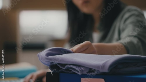 Young woman clothing store worker processes returned items, typing on laptop