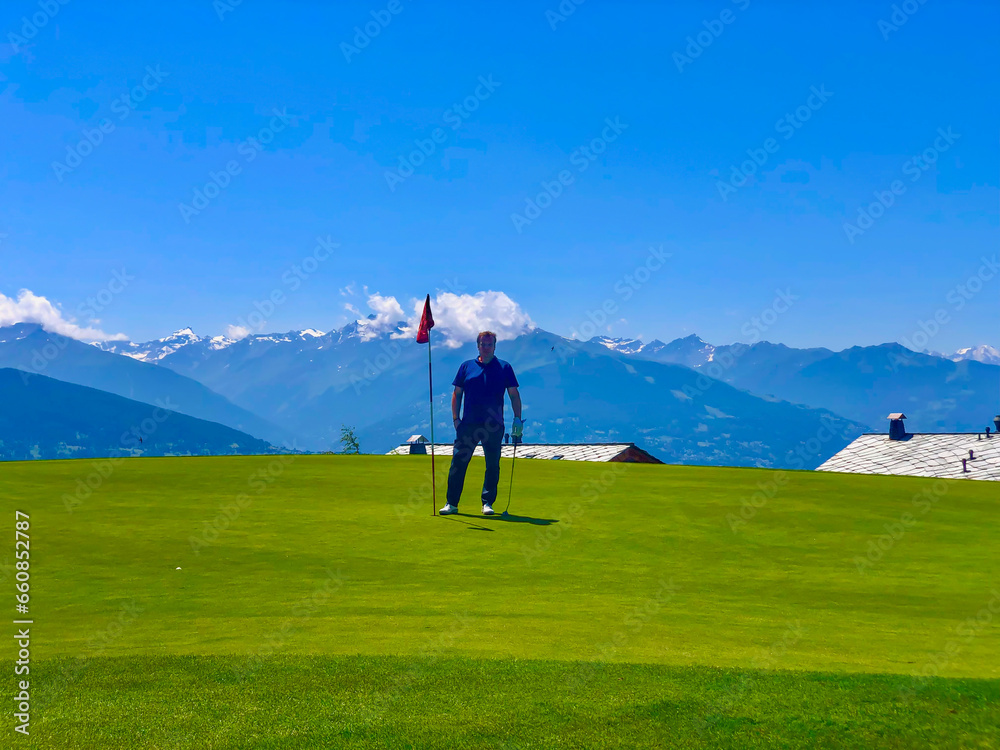 Golfer Standing on Putting Green in Crans Sur Sierre Golf Course with Hole 7 and Mountain View in Crans Montana in Valais, Switzerland.