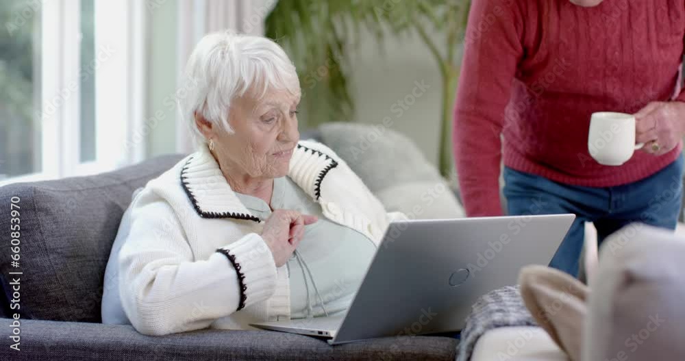 Happy senior caucasian couple sitting on sofa using laptop at home, slow motion Happy senior caucasian couple sitting on sofa using laptop at home, slow motion