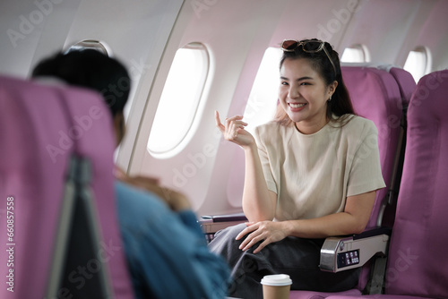 A couple of Asian tourists take photos of each other while sitting on a plane.