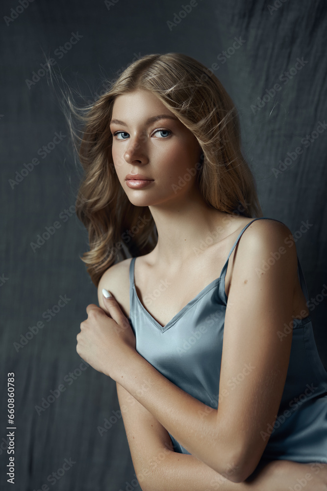 Portrait of a young woman in a light gray silk dress. Beautiful makeup, blue eyes of a blonde woman. Curly hair Portrait of a young woman in a light gray silk dress. Beautiful makeup, blue eyes of a blonde woman. Curly hair