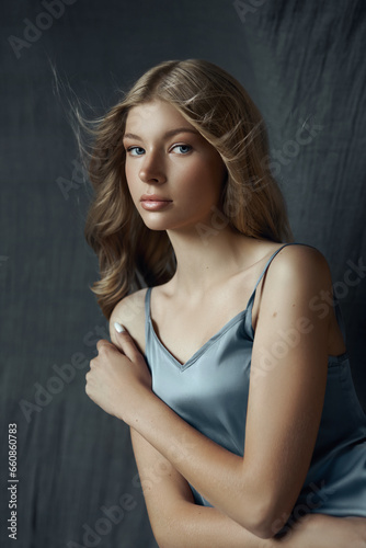 Portrait of a young woman in a light gray silk dress. Beautiful makeup, blue eyes of a blonde woman. Curly hair