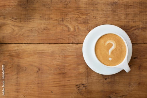 Top view of a cup of coffee with a question mark in the foam on a wooden table