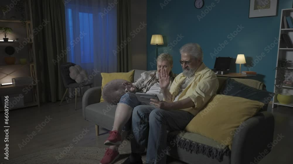 The frame shows an elderly couple sitting on a couch in an apartment. They are chatting passionately and joyfully with someone via video link from a tablet. HDR BT2020 HLG Material. The frame shows an elderly couple sitting on a couch in an apartment. They are chatting passionately and joyfully with someone via video link from a tablet. HDR BT2020 HLG Material.