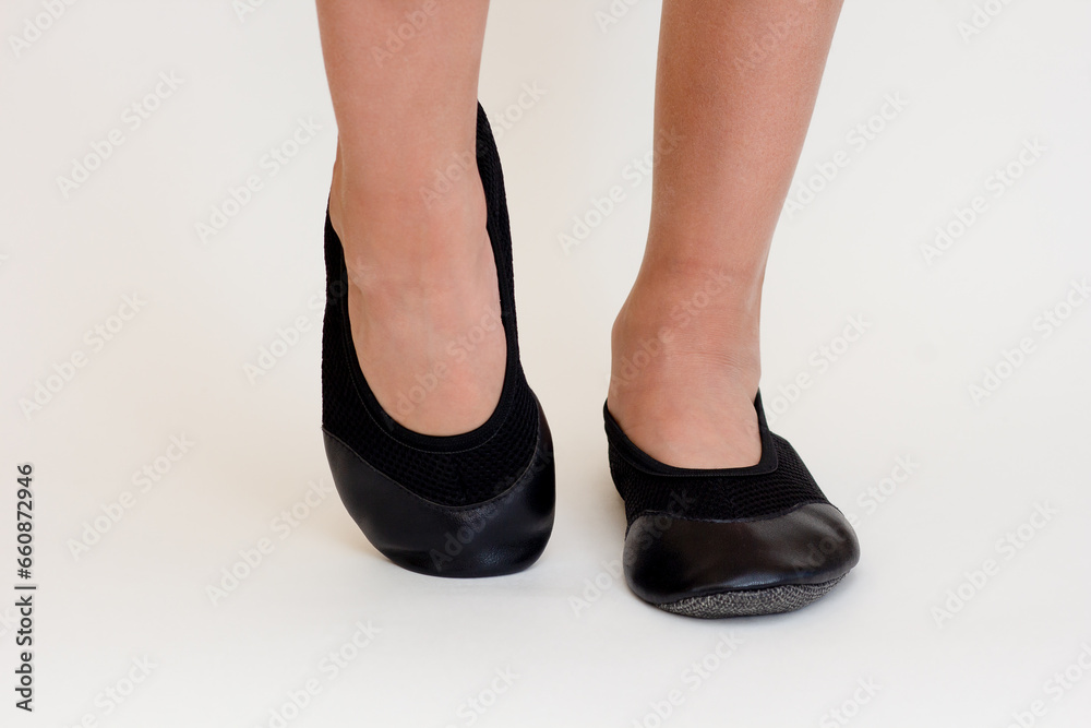 Cropped child legs in black leather ballet shoes on white background