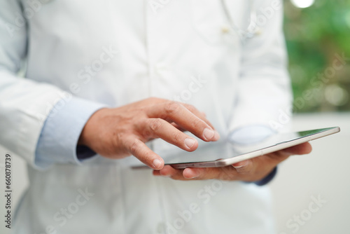 Asian man doctor using tablet computer to reading patient report, check up and search for solve treatment health medical online in hospital.