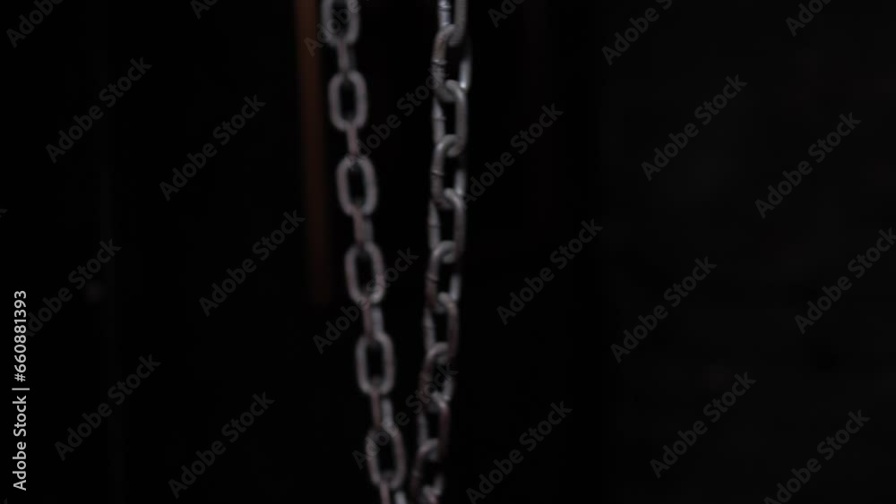Close-up of hanging metal chains in a dark room, chains swinging from side to side. Quest room or horror room. Close-up of hanging metal chains in a dark room, chains swinging from side to side. Quest room or horror room.