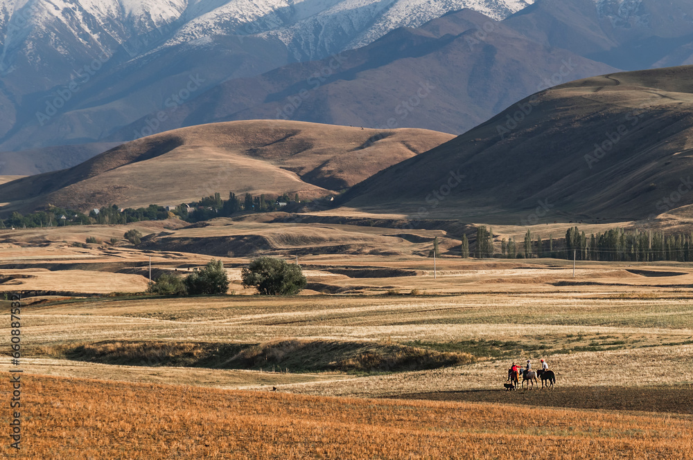 Obraz premium Mountains and rural life in Kyrgyzstan. In the distance are three young horsemen and a dog. Traditional means of transportation in Kyrgyzstan.