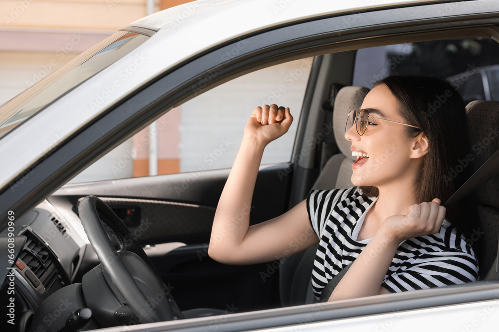 Listening to radio while driving. Beautiful young woman with stylish sunglasses enjoying music in car