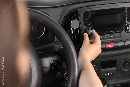 Listening to radio while driving. Woman turning volume button on vehicle audio in car, closeup © New Africa