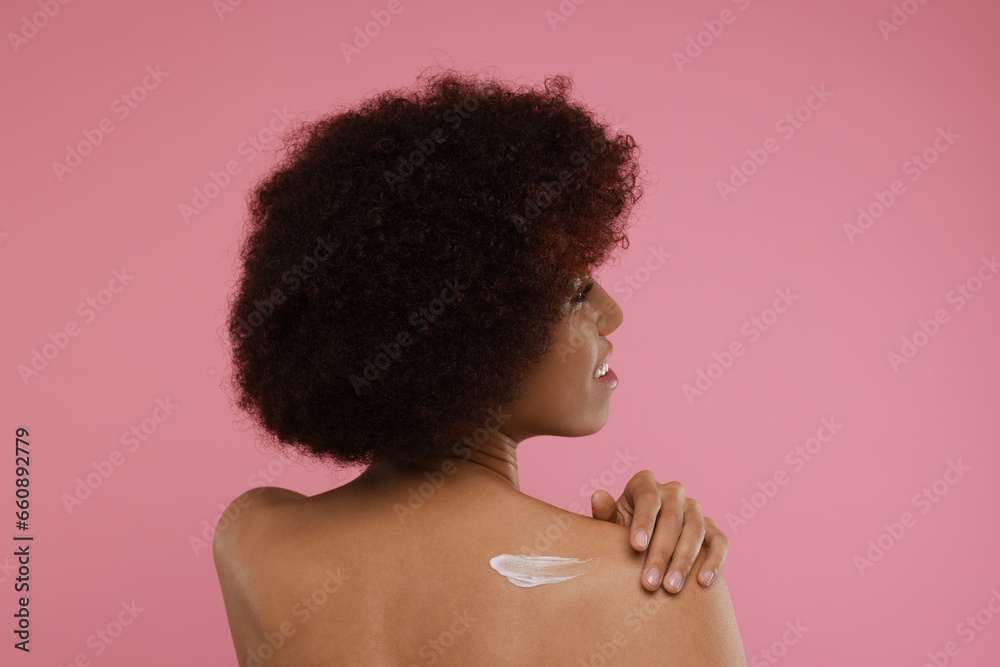 Beautiful young woman applying body cream onto back on pink background Beautiful young woman applying body cream onto back on pink background