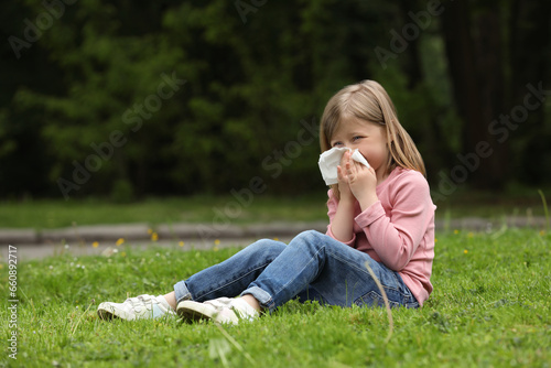 Little girl suffering from seasonal spring allergy on green grass in park