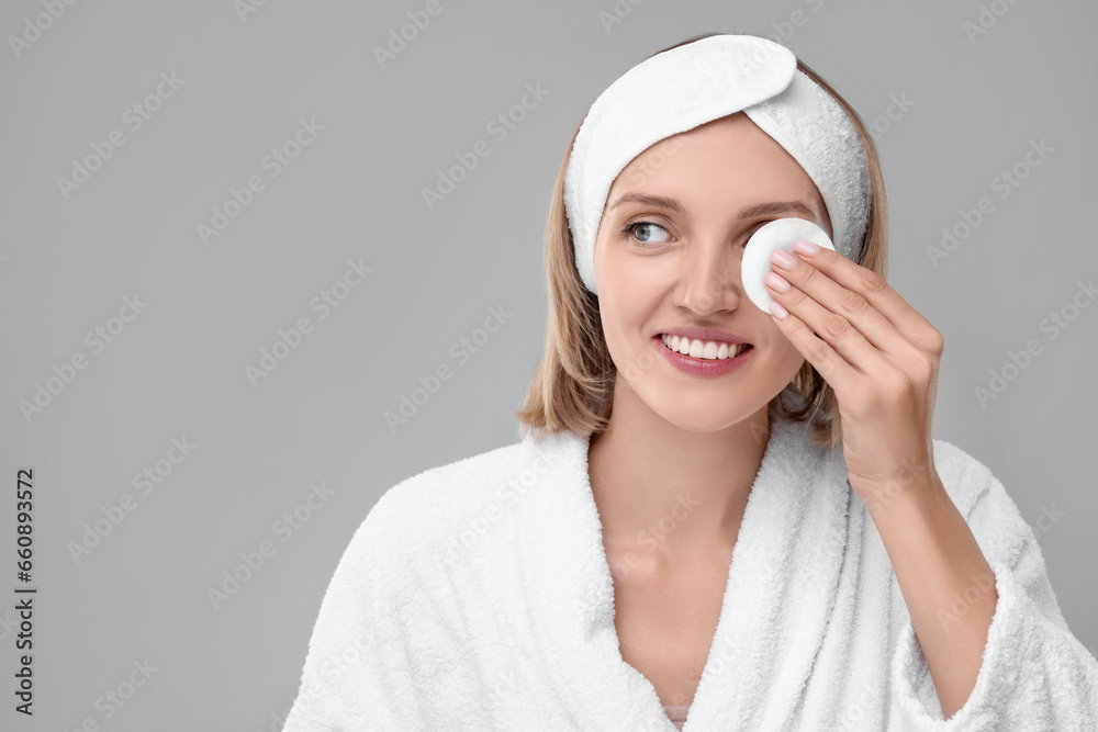Young woman cleaning face with cotton pad on light grey background. Space for text Young woman cleaning face with cotton pad on light grey background. Space for text