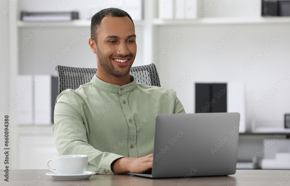 Handsome young man with laptop at table in office Handsome young man with laptop at table in office