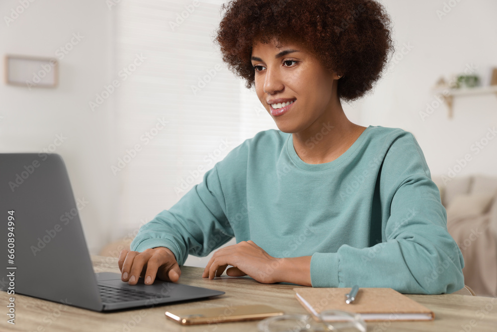 Young woman using laptop at wooden desk in room Young woman using laptop at wooden desk in room