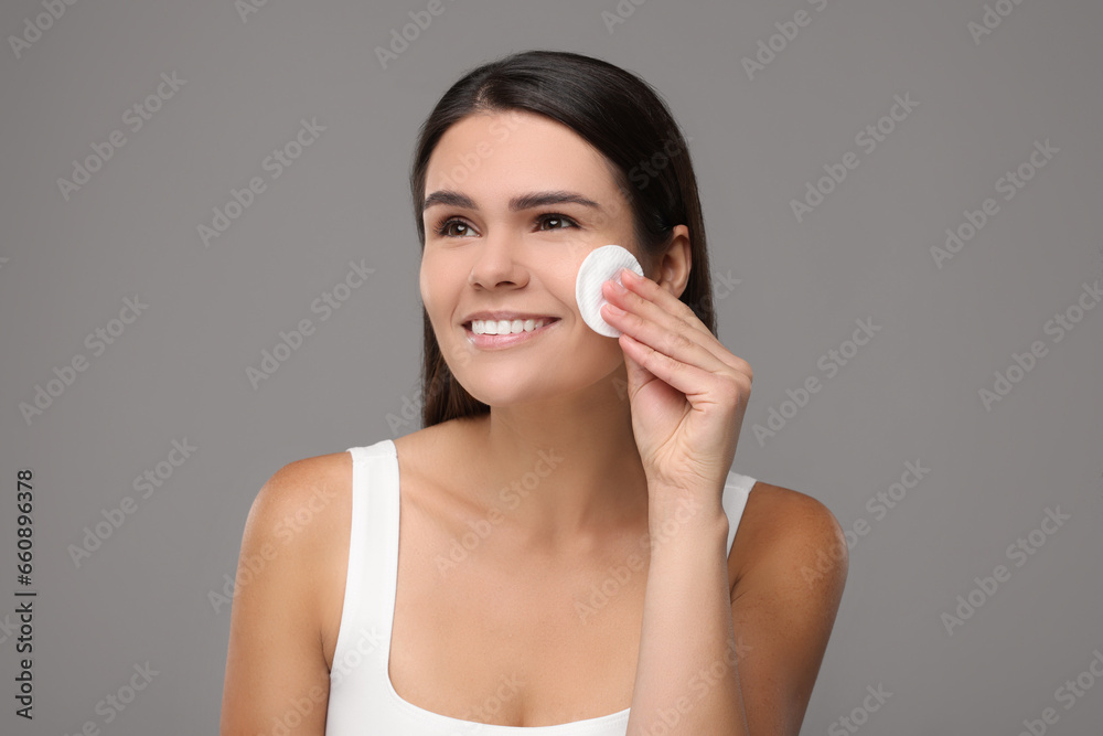 Young woman cleaning her face with cotton pad on grey background Young woman cleaning her face with cotton pad on grey background