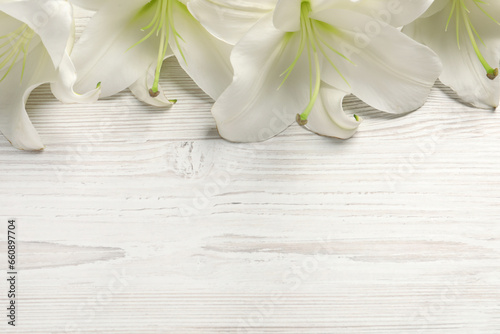 Beautiful lily flowers on white wooden table, flat lay. Space for text