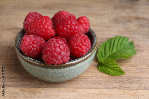 Tasty ripe raspberries and green leaves on wooden table, closeup