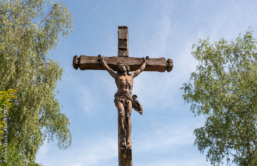 statue of jesus on cross between two trees against blue summer sky statue of jesus on cross between two trees against blue summer sky