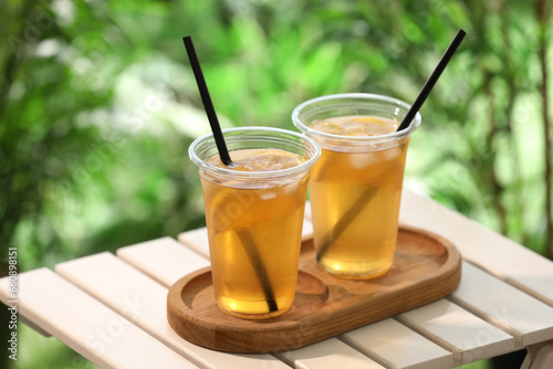 Plastic cups of tasty iced tea with lemon on white wooden table against blurred background