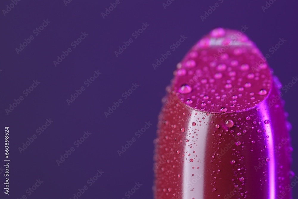 Lipstick with water drops on purple background, macro view. Space for text Lipstick with water drops on purple background, macro view. Space for text