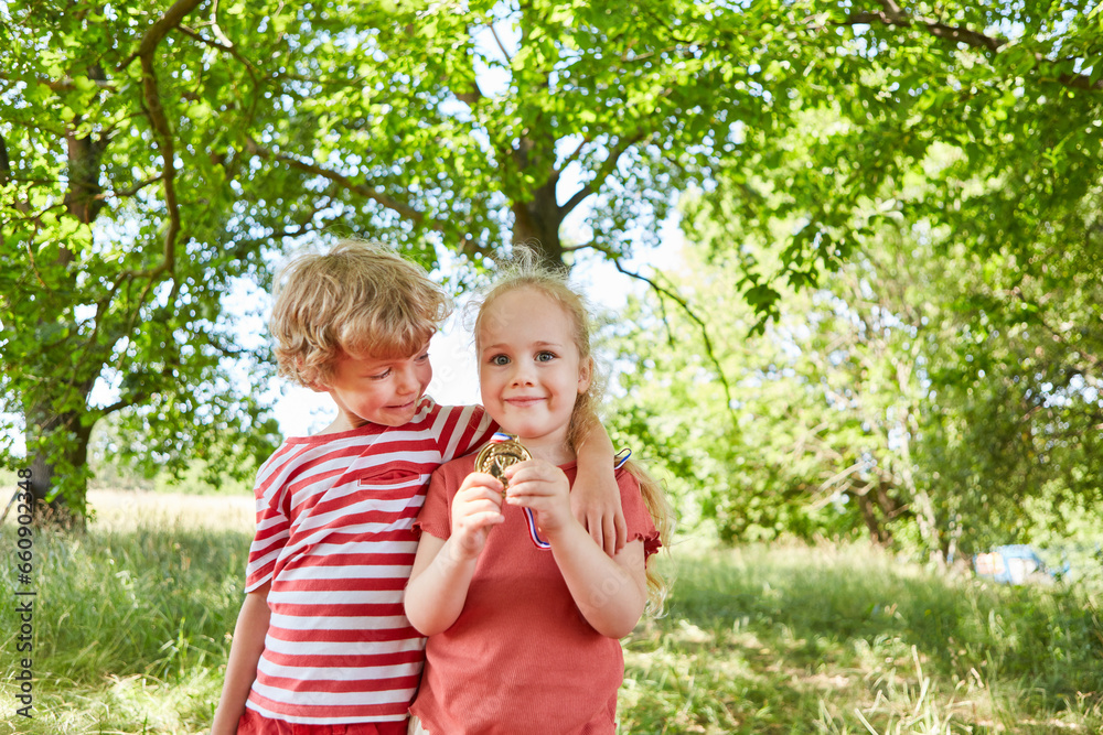 Obraz premium Boy looking at sister showing medal in garden