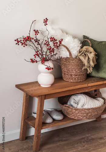 Cozy autumn winter season interior - wooden bench with cranberry branches in a ceramic vase, baskets with blankets, pillow