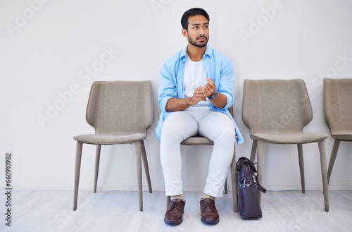 Waiting room, recruitment and man in an office for interview in job search for appointment. Hiring, career and Indian male person sitting on chair for meeting with human resources in modern workplace