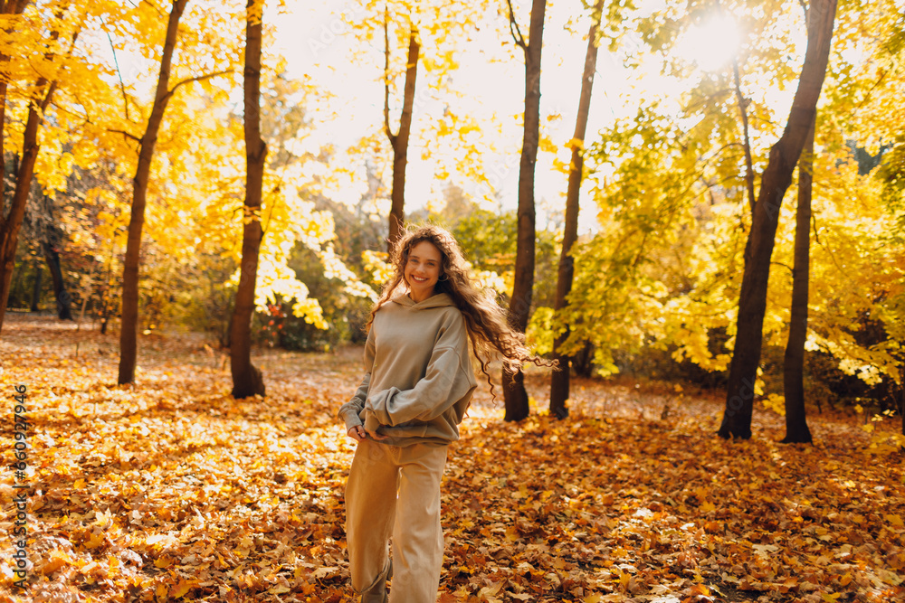 Smiling young woman plays and jumping dancing in the autumn forest with the yellow leaves at sunset Smiling young woman plays and jumping dancing in the autumn forest with the yellow leaves at sunset