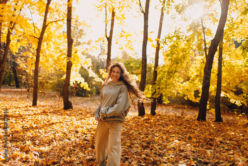 Smiling young woman plays and jumping dancing in the autumn forest with the yellow leaves at sunset