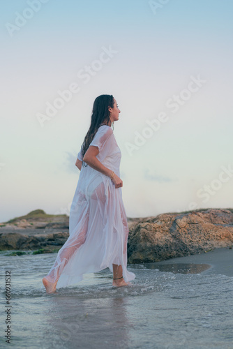 Young beautiful woman runs on a seashore at sunset
