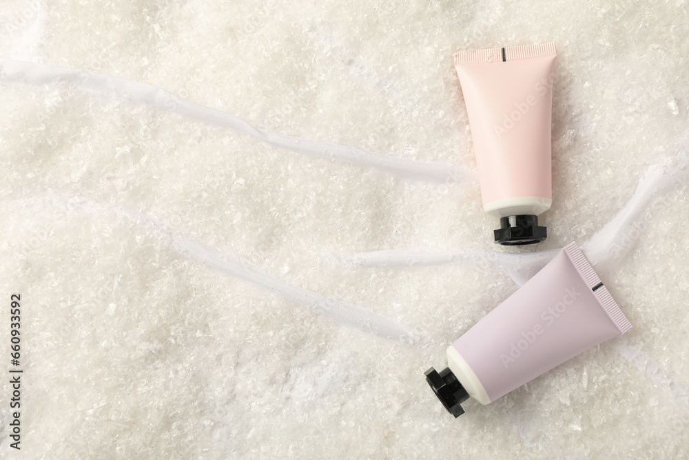 Cosmetic tubes and snow on light background, space for text