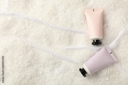Cosmetic tubes and snow on light background, space for text