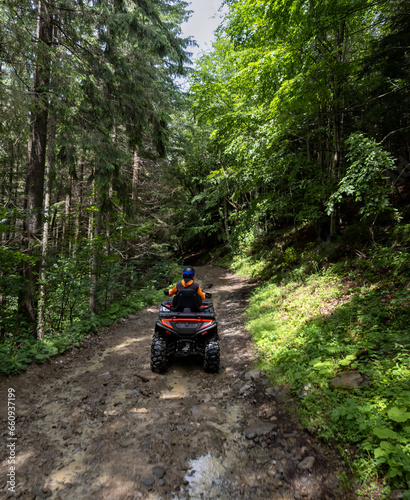 A man in a helmet and overalls rides an ATV along a forest path. Vacation and adventure concept