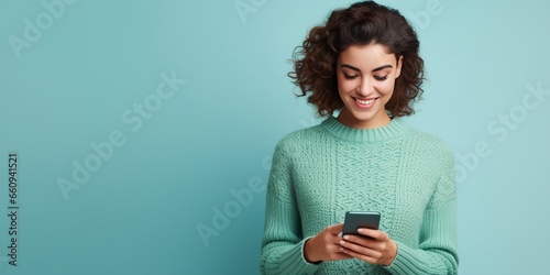 Full body fun young woman wear knitted sweater hold in hand use mobile cell phone look aside on workspace isolated on plain pastel light blue cyan background studio portrait. People li : Generative AI photo