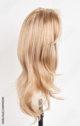 Natural looking blonde wig on white mannequin head. Long hair on the plastic wig holder isolated on white background, side view.