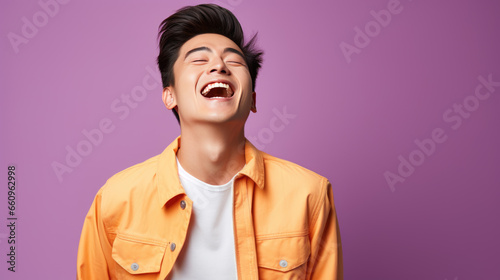 Young man laughs against a purple background.