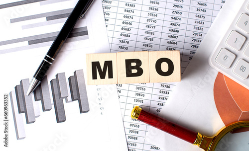 MBO text on wooden block on graph background with pen and magnifier photo