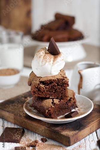 Brownie sliced ​​with a scoop of ice cream on top with a piece of chocolate. In the background is a northerly table with milk and the rest of the brownies.