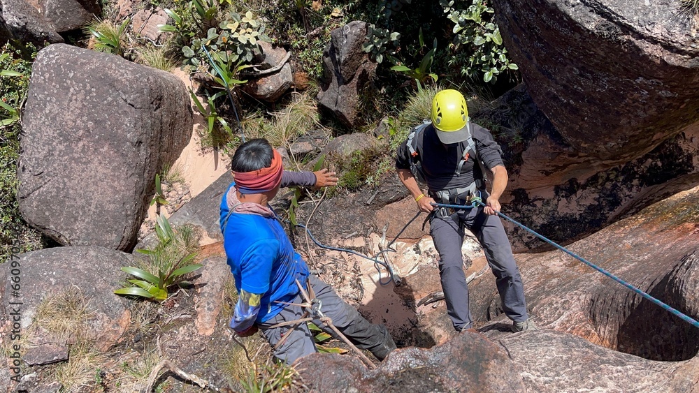 Hiker in safety harness and helmet climbing down a rope from rocky ...