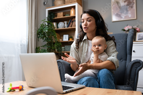 Female business owner work on laptop from home during maternity leave, running private company with baby in her lap, having online video call. Businesswoman mother with toddler working at the computer