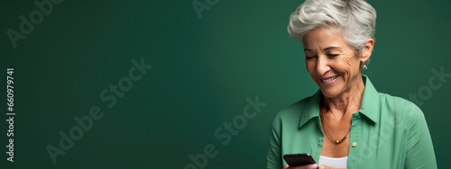 An elderly woman smiling and laughing with her phone against a colored background.