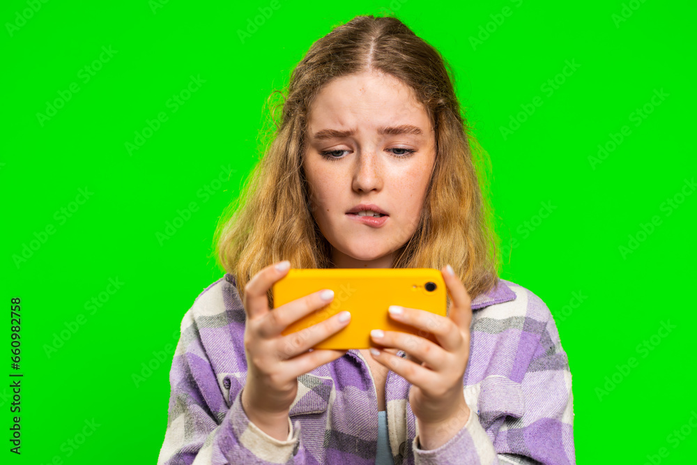 Worried young caucasian woman enthusiastically playing racing drive simulator or shooter video games on smartphone. Happy redhead girl player celebrate victory isolated on green chroma key background Worried young caucasian woman enthusiastically playing racing drive simulator or shooter video games on smartphone. Happy redhead girl player celebrate victory isolated on green chroma key background
