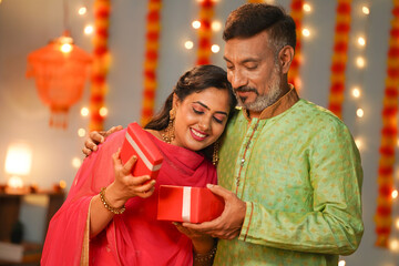 Happy senior father giving surprise gift to daughter at diwali festival celebration at home - concept of special occasion, family festive ceremony and relationship bonding.