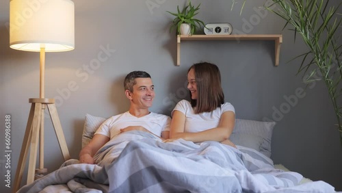 Cheerful happy young woman looking under covers man partner genitals being pleasantly surprised having satisfied expression of seeing husband erection.