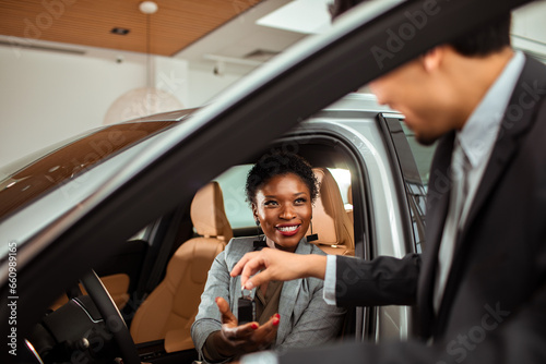 Young African American woman receiving the keys of the car she bought at the dealership